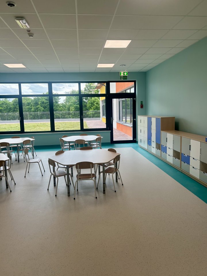 Sala przedszkolna urządzona w kolorystyce niebieskiej. W centralnej części pomieszczenia znajdują się małe, dziecięce stoliki i krzesełka.