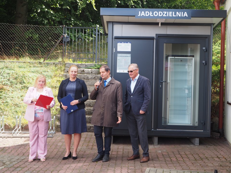 Zdjęcie przedstawia cztery dorosłe osoby stojące przy jadłodzielni.